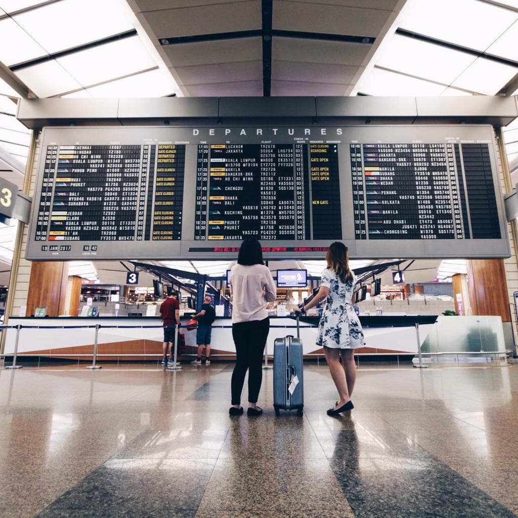 Travelers with a suitcase checking the departures board at the airport